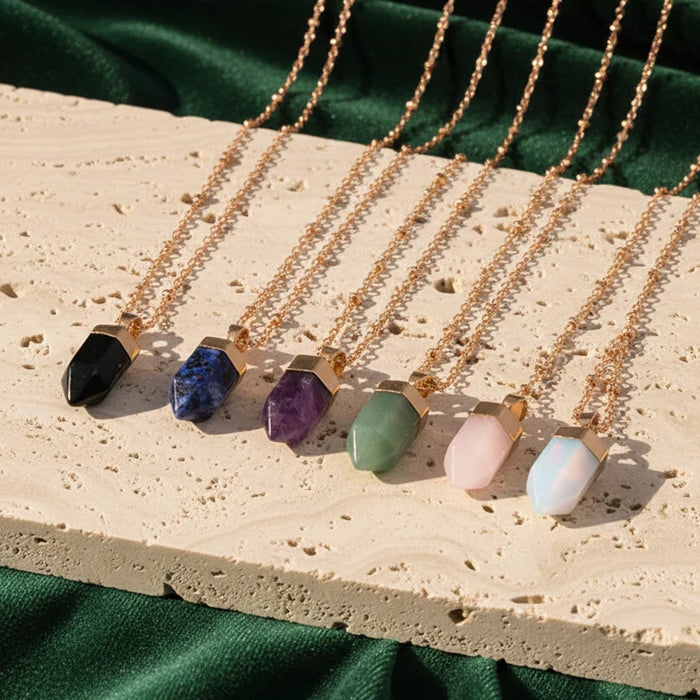 Six crystal pendants in graded colours from black through blue and purple to pink, laid in a row on pale stone over green velvet