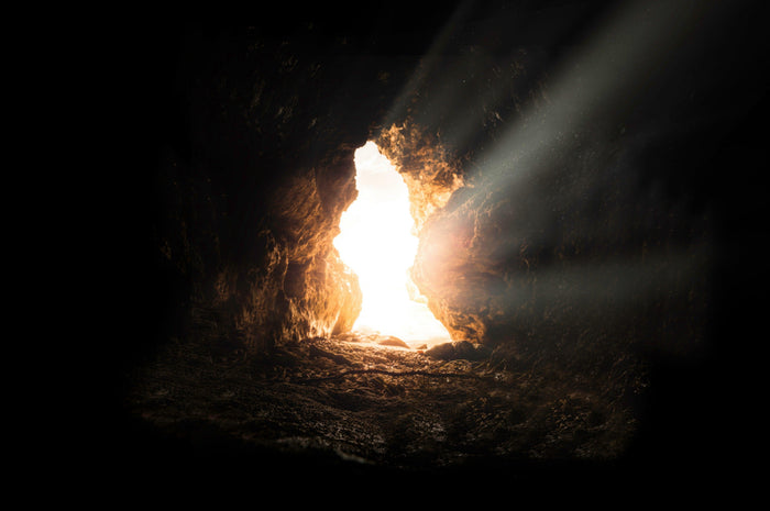 Sunlight streaming through a cave mouth into a dark underground chamber, the classic image of the inner descent