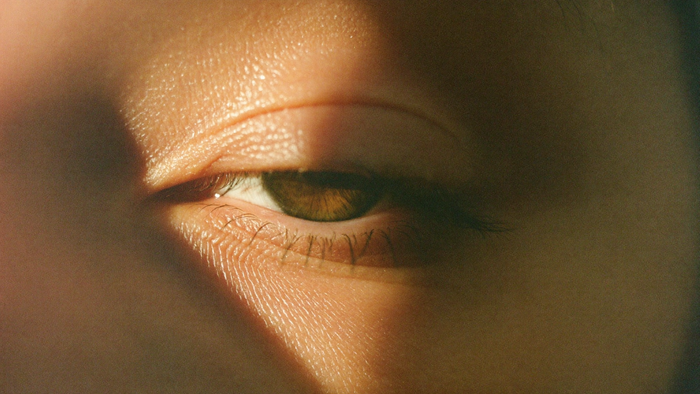 Close-up of a human eye with the upper eyelid half lowered, lit by warm candlelight from the left side