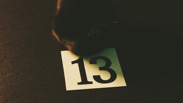 A black cat's paw beside a small white card printed with the number 13, lit by warm candlelight