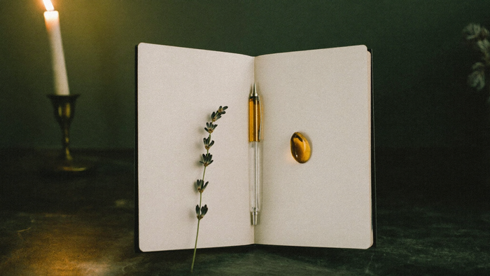 Open blank journal with a pen, a lavender sprig and an amber stone beside a lit candle.