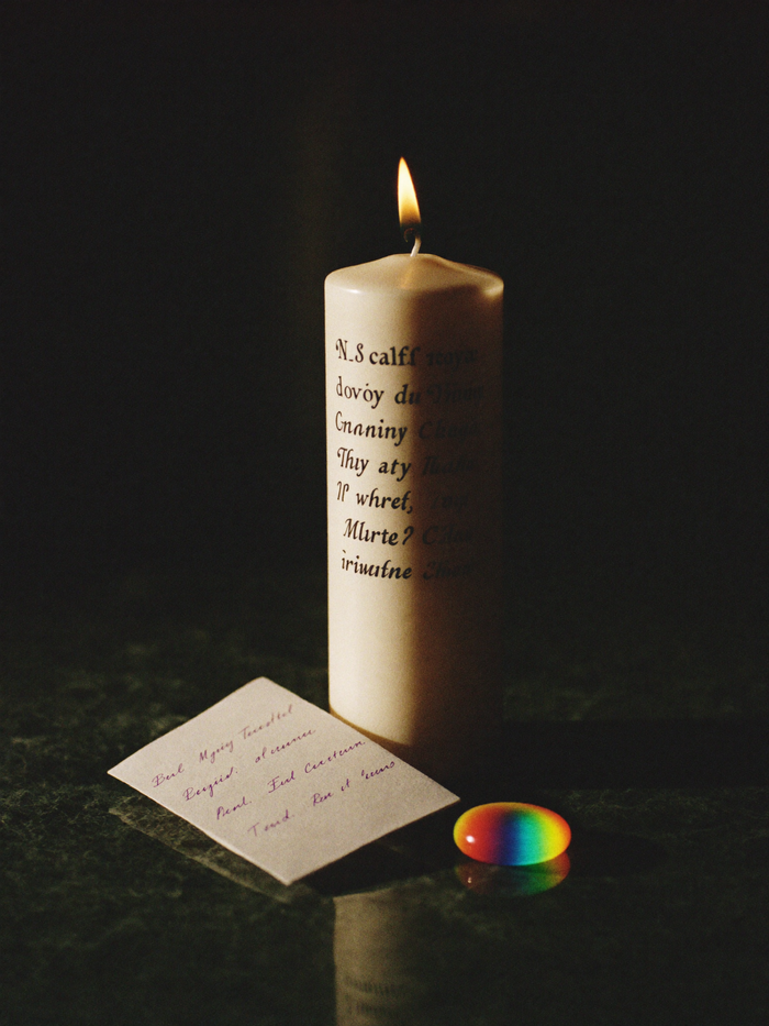 A seven-day glass ritual candle set for New Moon work, standing on polished dark marble with a deep emerald-green background falling softly into shadow.