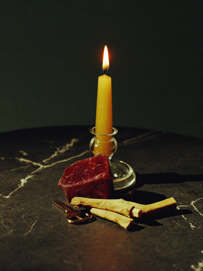 A road opener candle and a money candle standing together on polished dark marble against a deep emerald-green background falling into shadow.