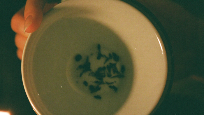 Wet tea leaves scattered in patterns inside a pale porcelain cup held by candlelight