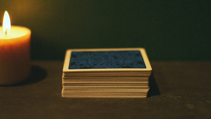 A face-down Lenormand deck stacked on a dark wooden table beside a lit pillar candle in warm light