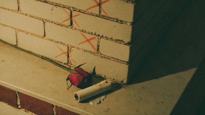 Hand-drawn X marks on the whitewashed brick of an old New Orleans tomb with a red rose and a candle stub