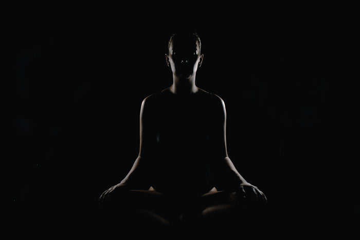 Silhouette of a person sitting cross-legged in meditation against a dark background