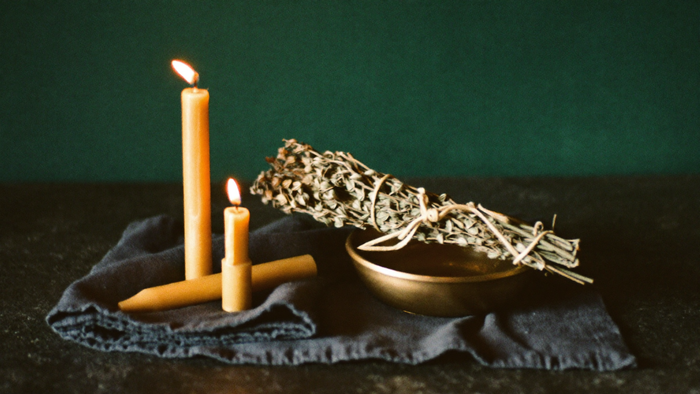 Beeswax candles, a brass bowl and a bundle of dried herbs resting on a folded dark cloth, packed ready to move