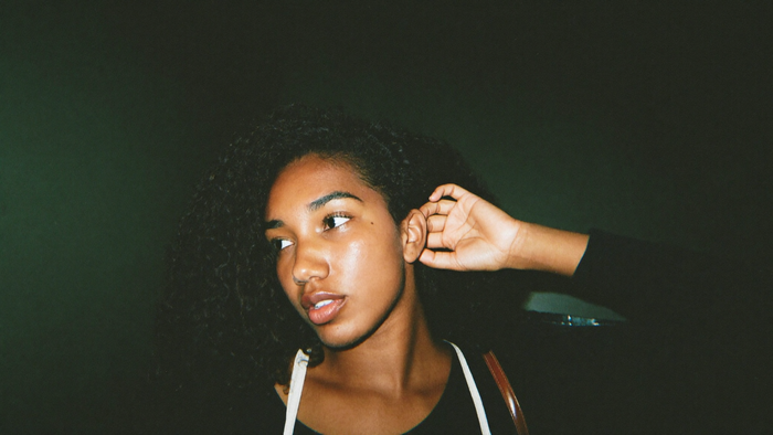 A young woman cups her hand behind her ear and listens, head turned toward a faint sound