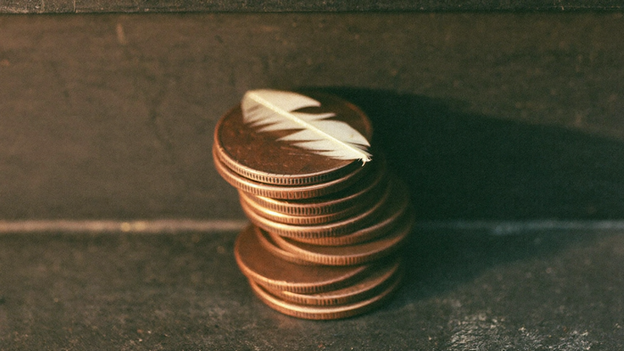 Stack of old copper pennies with a small white feather resting on top, lit by warm candlelight