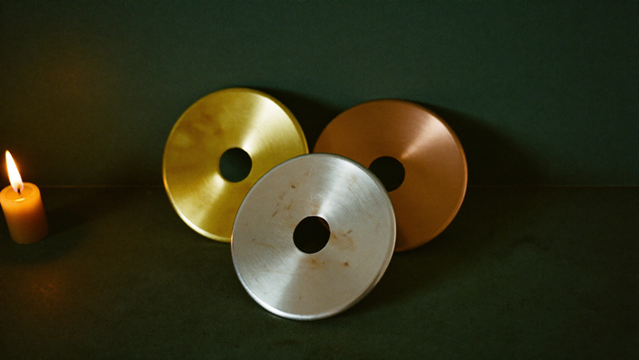 Three metal discs in gold, silver and copper standing in candlelight against a dark green wall