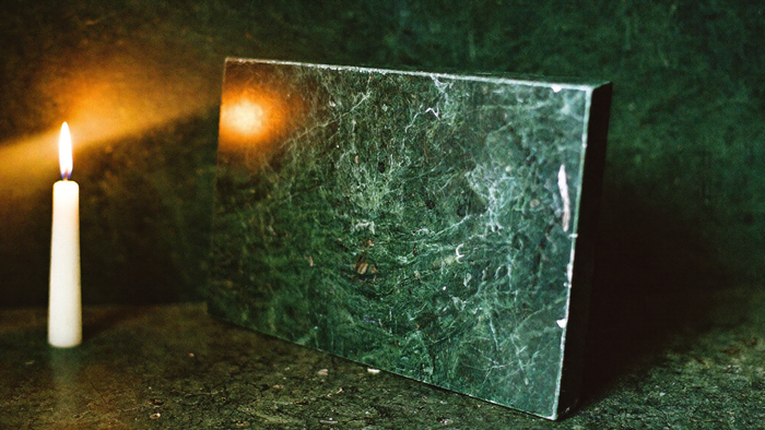 Polished dark green stone slab standing upright beside a lit candle against a green wall