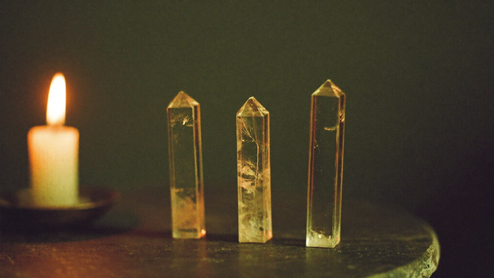Three clear quartz points standing in a row on dark stone beside a burning candle