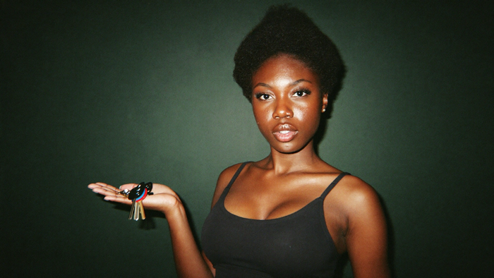Young woman holding a set of house keys in her open palm against a dark green wall