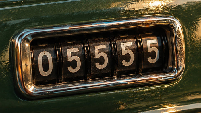 Close-up of a classic car's mechanical odometer drum reading 05555 in white digits, chrome bezel, green dash