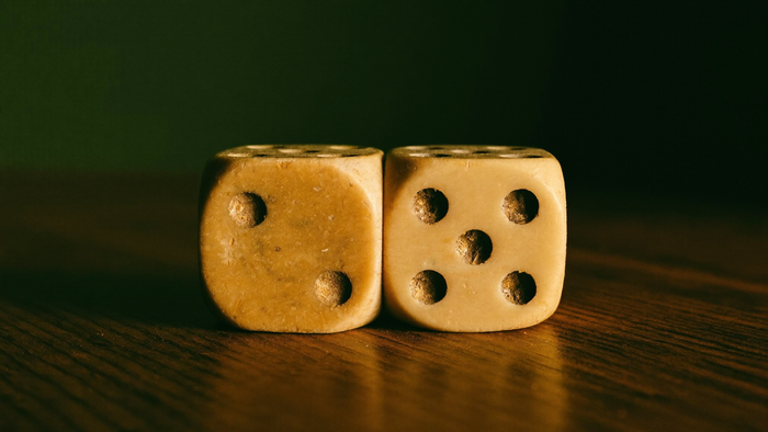 Two old ivory dice on a dark oak table showing two pips and five pips, together making seven