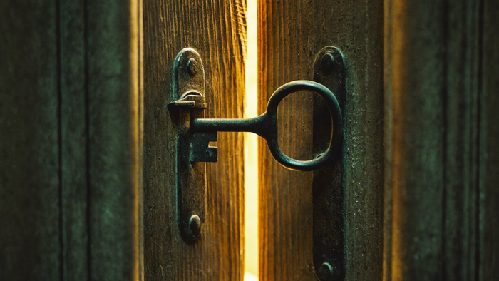 Old iron key resting in the lock of a weathered wooden door that stands slightly ajar, warm light spilling through the gap