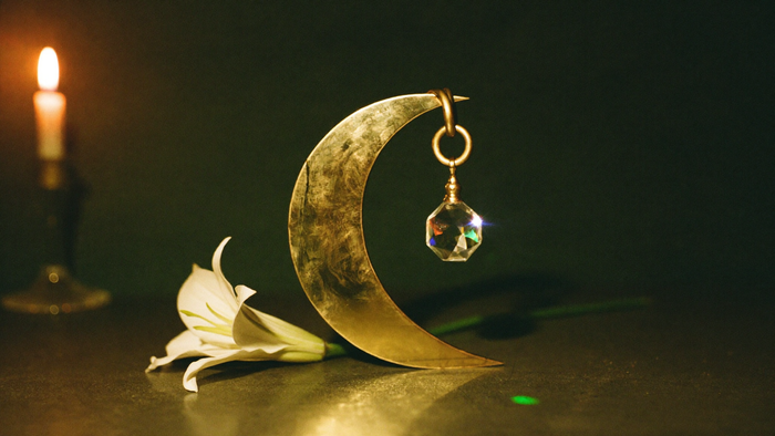 Brass crescent moon with a hanging faceted crystal and a white lily on dark stone