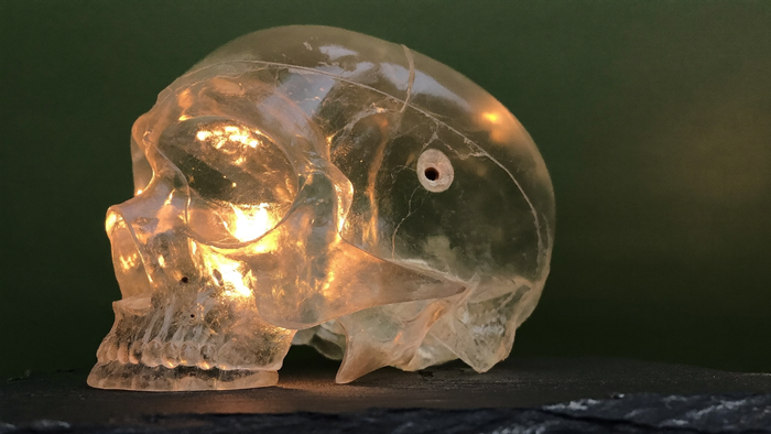 Carved clear quartz crystal skull lit by warm candlelight on dark slate, macro detail