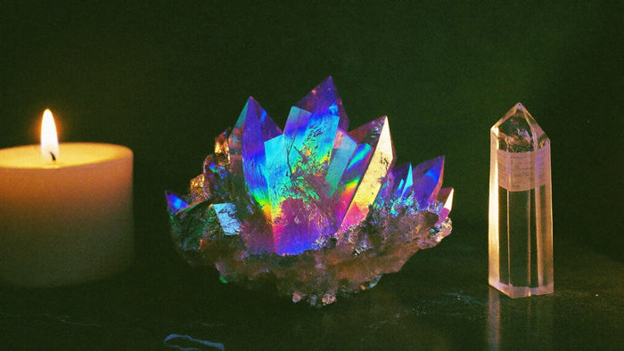 Titanium aura quartz cluster glowing in rainbow colors beside an uncoated clear quartz point and a lit candle
