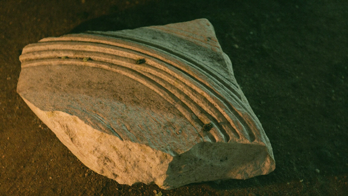 Carved limestone fragment from an abbey vault lying on dark earth in warm candlelight