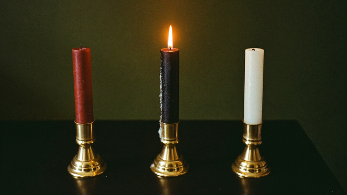 Three colored ritual taper candles in brass holders on dark stone, the black one lit