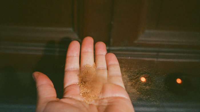 Open palm blowing ground cinnamon across a dark wooden door threshold in warm candlelight
