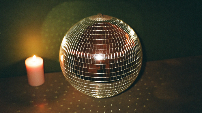 A mirror ball on a dark surface beside a burning candle, scattering points of light across a green wall