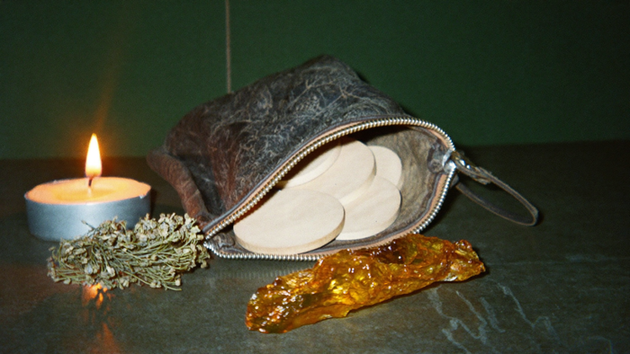 Open leather pouch spilling blank wooden rune discs beside dried herbs, a piece of raw amber and a lit candle