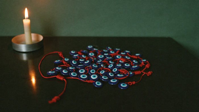 Blue nazar eye beads on red cords spread on a dark altar table beside a burning candle