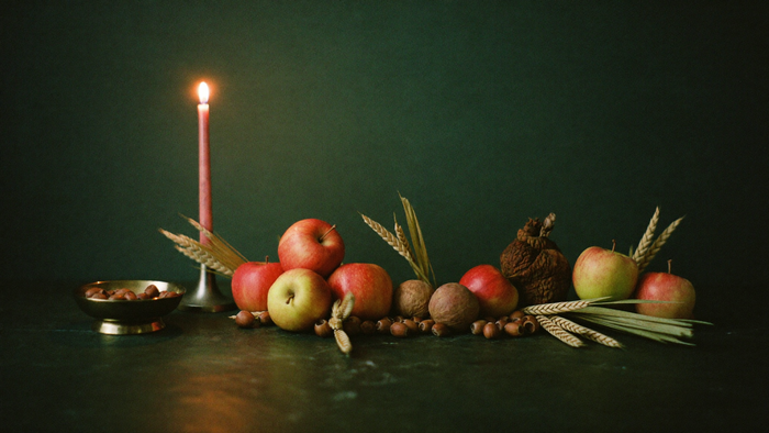 Apples, wheat stalks, hazelnuts and walnuts on dark stone beside a burning candle and a brass bowl