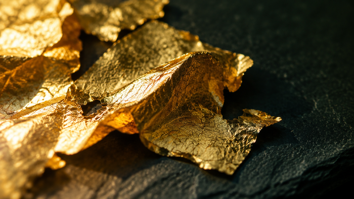 Crumpled sheets of gold leaf catching warm light on a dark slate surface