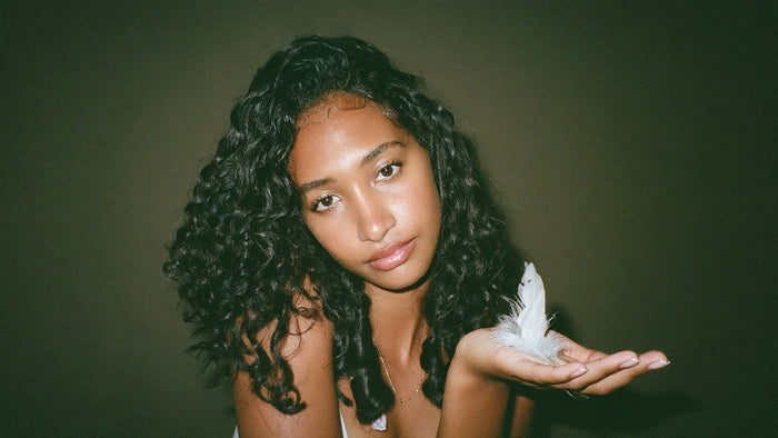 A young woman holding a single soft white feather in her open palm against a dark green wall