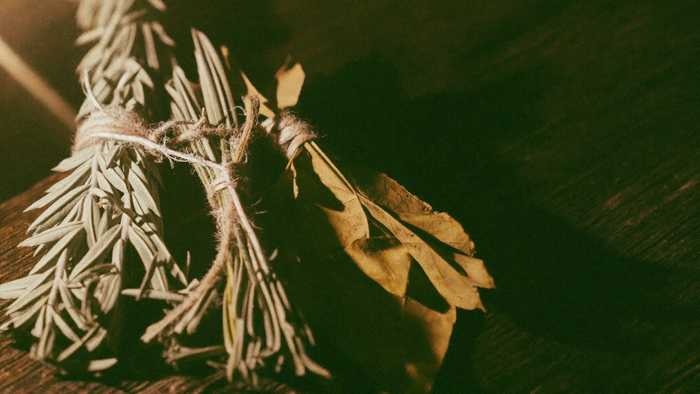 Bundles of dried rosemary, mugwort and bay leaves tied with twine on dark wood in warm candlelight