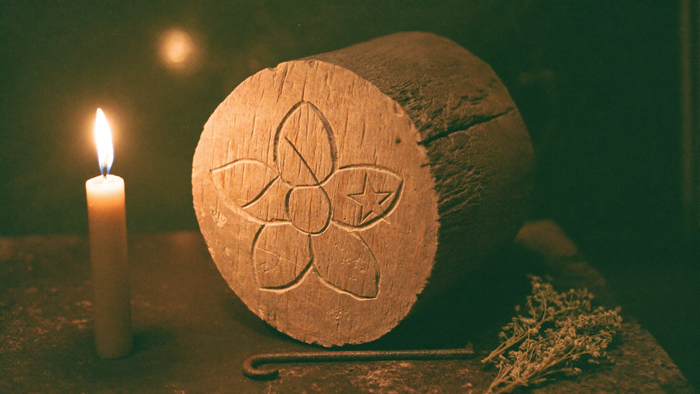 Hexafoil daisy wheel carved into the end of an old oak beam, lit by a single candle