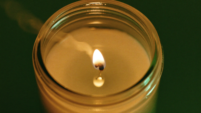 Seen from above, a burning seven-day glass candle with the flame on its wick in a clear pool of melted wax