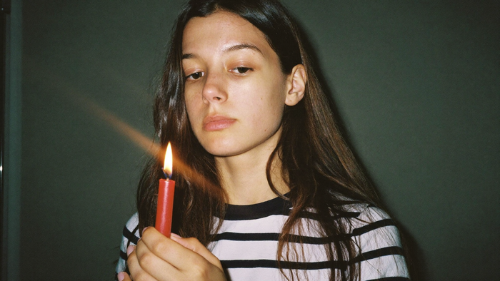Young woman studying the flame of a small red candle against a dark green wall