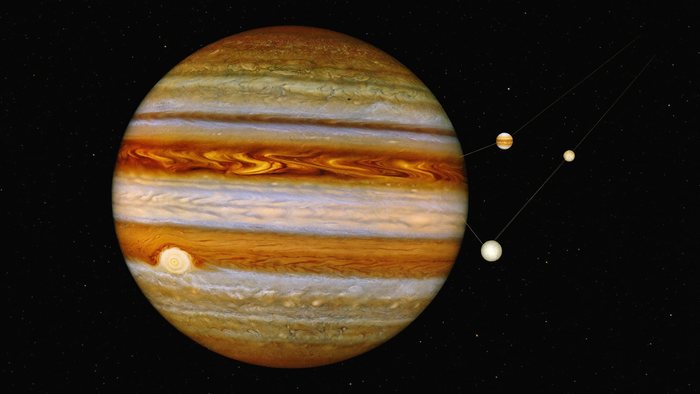 The planet Jupiter as a full disc with cream and rust cloud bands and three small moons strung out beside it against black space