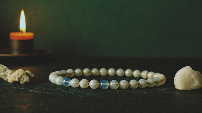 Moonstone bead bracelet showing blue schiller beside two raw stones on dark stone