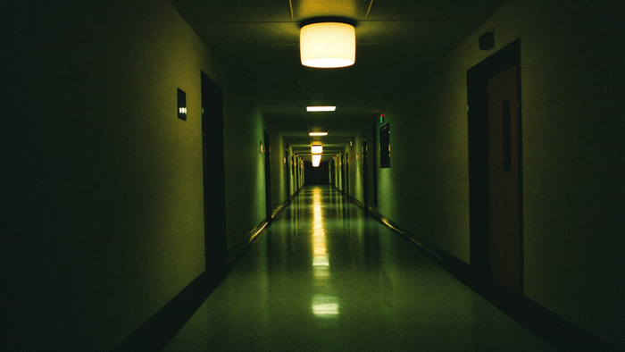 Empty hospital corridor at night, a single warm ceiling lamp above the polished floor