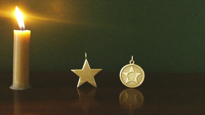 Brass five-pointed star pendant beside a round pentacle disc pendant on dark wood in candlelight