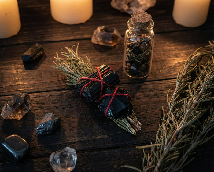 Black tourmaline and obsidian bound with red cord beside a corked jar of black salt and rosemary on dark wood