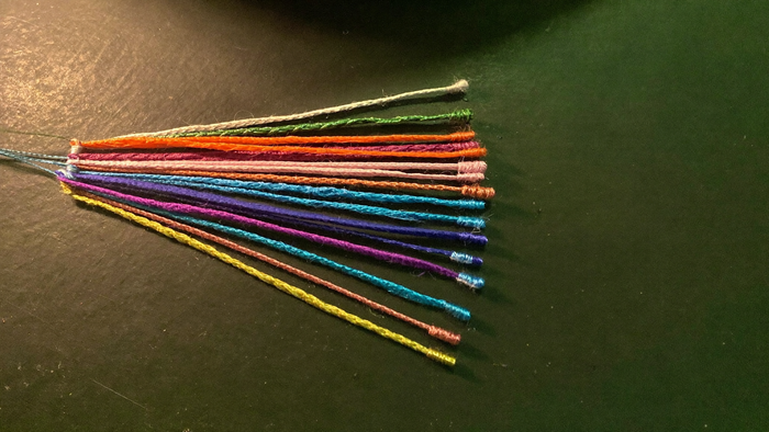 Dyed cords in many colors fanned out from a single point across a dark green surface