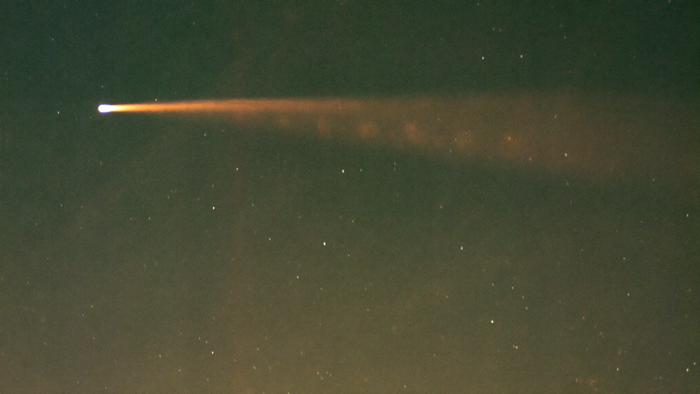 A single meteor with a bright head and a long fading tail crossing a dark star-scattered night sky
