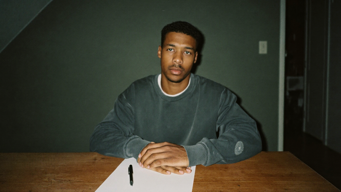 Young man sitting at a bare wooden table with a blank sheet of paper and a pen before a ritual