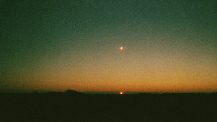 A single bright point of light in a green and amber twilight sky above a dark low horizon
