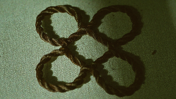 Knot of dark cord tied into four interlaced loops resting flat on coarse natural linen in morning light