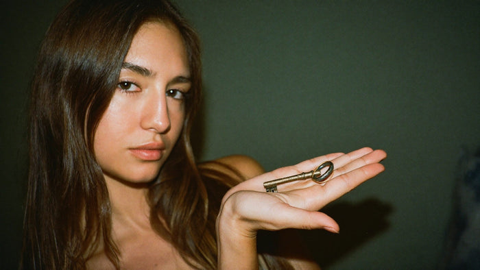 A young woman holds an old brass key flat in her open palm against a dark green wall