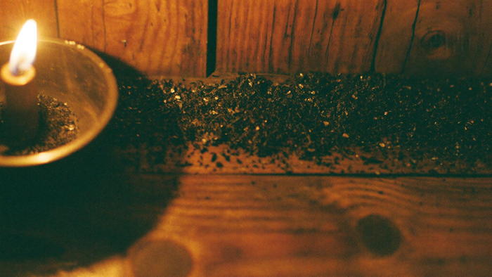 A line of coarse dark salt laid across a worn wooden threshold, lit by a candle at the left