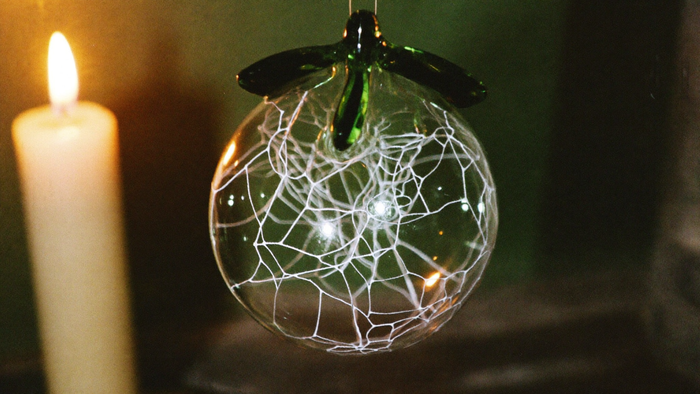 Hand-blown glass witch ball with a web of white glass threads, hanging by candlelight